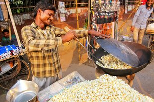 Strassenverkäufer röstet Popcorn in einem dunklen Tigel