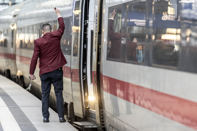 Zugschaffner steht auf einem Bahnhof neben ICE