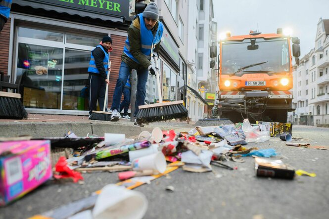 Ein Mann fegt auf einer Straße Böllerüberreste weg