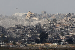 Blick auf eine ehemalige Stadt in Gaza. Viele Häuser sind eingestürzte Ruinen. Ein besonders hohes Haus weit hinten steht schief in den Himmel.