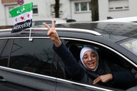 Eine Frau schaut aus einem Autofenster. Sie macht das Siegeszeichen, am Auto weht die Fahne der syrischen Opposition