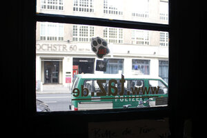 Blick aus dem Fenster in der Haustür der taz in der Rudi-Dutschke-Straße. Vor dem Haus steht ein grüner Polizeibulli. Auf dem Fenster klebt eine tazze und die URL der taz