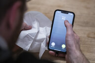 Ein Mann hält ein Taschentuch in einer Hand und ein Telefon mit dem Schriftzug "Besetzt Arzt" in der Anderen.