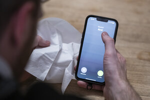 Ein Mann hält ein Taschentuch in einer Hand und ein Telefon mit dem Schriftzug 