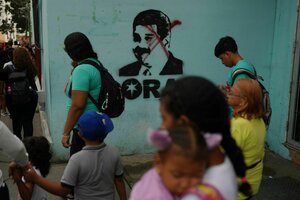 Passanten auf einer Straße, Maduro-Porträt auf einer Wand ist druchgestrichen