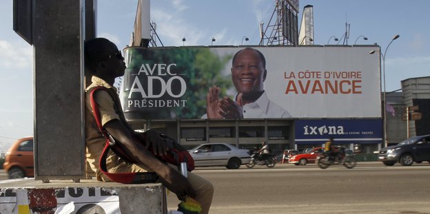 Ein junger Mann sitzt vor einem großen Wahlplakat