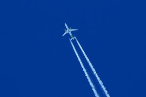 Ein Flugzeug zieht Kondensstreifen vor blauem Himmel hinter sich her