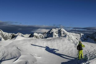 Schneebedeckte Gipfel in Österreich, ein Tourengeher von hinten zu sehen, der einen großen Schatten wirft