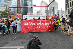 Demonstranten tragen ein Plakat mit der Aufschrift "Die Miete ist zu hoch!".