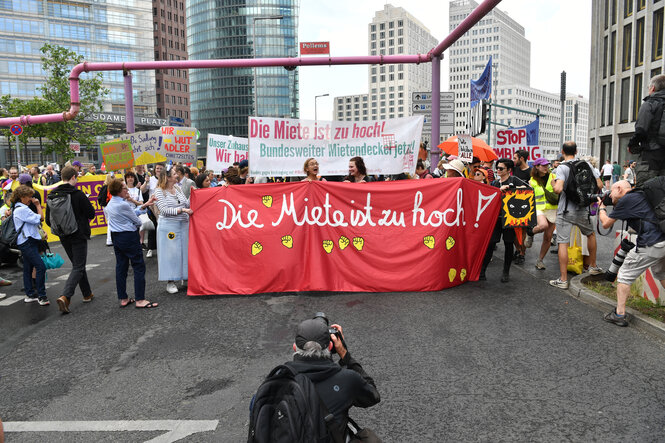 Demonstranten tragen ein Plakat mit der Aufschrift "Die Miete ist zu hoch!".