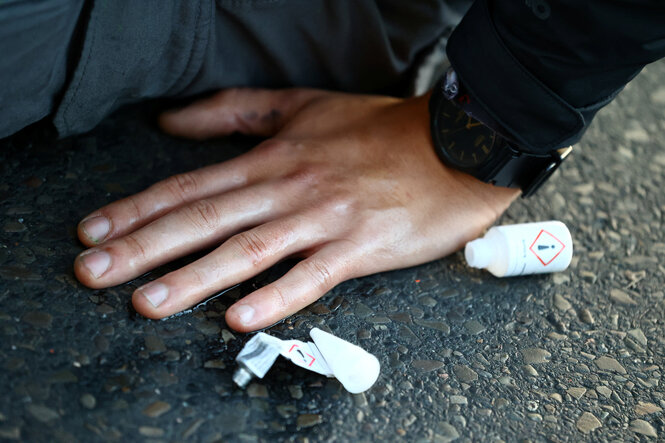 Klebstofftube neben einer festgeklebten Hand auf Strassenpflaster