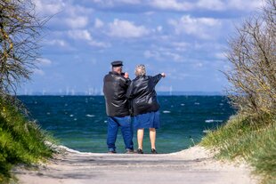 Ein alter Mann schaut durch ein Fernglas, eine Frau zeigt aufs Meer