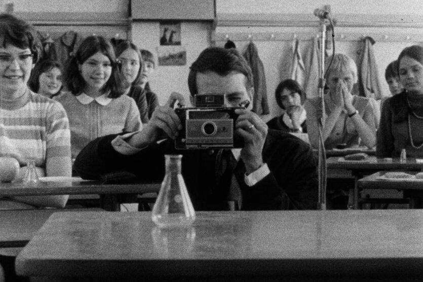 Regisseur Edgar Reitz sitzt in der histo­rischen „Filmstunde“ von 1968 zwischen Schülerinnen im Klassenzimmer und eine Kamera vors Auge.