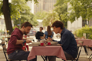 Benji (Kieran Culkin, l.) und David (Jesse Eisenberg) sitzen draußen an einem Restaurant-Tisch und essen