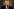 Donald Trump spricht in ein Mikrofon. Er ist ein sehr alter Mann mit rotorangener Haut. Sein lichtes Haar hat er sich über die Halbglatze gekämmt.