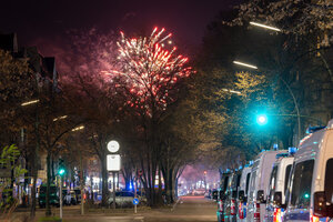 Fahrzeuge der Polizei stehen in der Sonnenallee im Stadtbezirk Neukölln in der Verbotszone für Feuerwerk. Im Hintergrund außerhalb der Zone ist am Himmel Feuerwerk zu sehen.