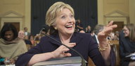 Hillary Clinton lacht, vor ihr liegt ein Aktenordner