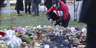 Ein Mann kniet vor Blumen und Kerzen, die auf dem Boden liegen