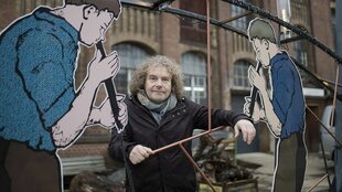 Portrait von Torsten Pötzsch vor der Glasfabrik in Weiswasser. Ersteht zwischen stilisierten Figuren, die Glasbläser darstellen.