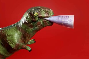 Spielzeug Dinosaurier mit 500 Euro Note in seinem Maul auf rotem Hintergrund