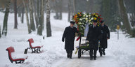 Friedhofsmitarbeiter bringen Blumenkränze zu einem Grab