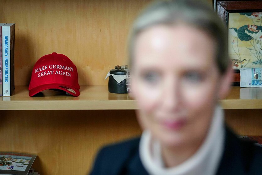 Unscharfes Porträt v on Alice Weidel, hinter ihr ein Regal in dem ein Basecap liegt mit der aufschrift: