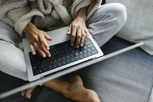 Eine Person im Pyjama sitzt mit einem Laptop auf dem Boden