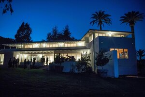 Eine Menschengruppe steht im Garten eines beleuchteten Hauses bei Nacht