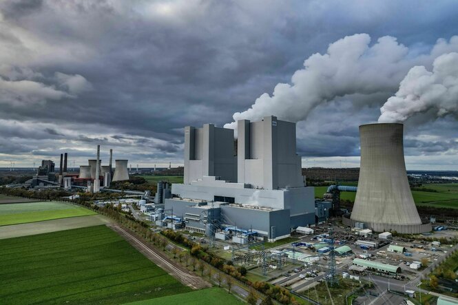 Dampf steigt aus dem Braunkohlekraftwerk Neurath, zu sehen sind Kühltürme und die gigantische Kraftwerksanlage von oben. Dunkle Wolken am Himmel