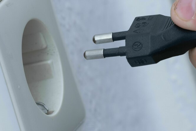 Ein Mensch steckt einen Stecker in eine Steckdose