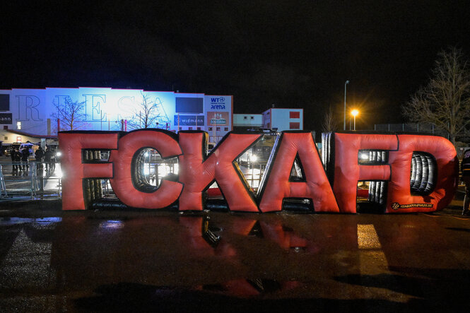 Aufblasbare Riesenbuchstaben stehen auf einem nächtlichen Parkplatz. Sie bilden den Slogan: „FCKAFD“