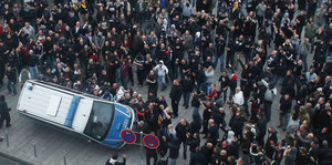 Umgeworfener Polizeibus in einer Menschenmenge