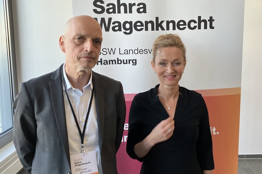 Zaklin Nastic mit Konstantin Eulenburg stehen vor einer Plakatwand mit der Aufschrift "Bündnis Sahra Wagenknecht"