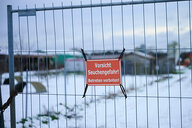 Zaun mit Warnschild "Vorsicht Seuchengefahr" vor verschneiter Landschaft