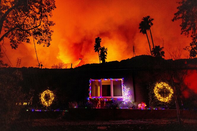 Ein Hubschrauber wirft Wasser auf das „Palisades Fire“ hinter einem Haus mit Weihnachtsbeleuchtung im Mandeville Canyon ab.