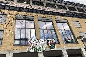 Die Fassade eines großen Gebäudes, aus Fenstern hängen Transparente mit der Aufschrift „Friede der Welt, Tod dem Imperialismus“ sowie „ASH ist besetzt Free Palestine“