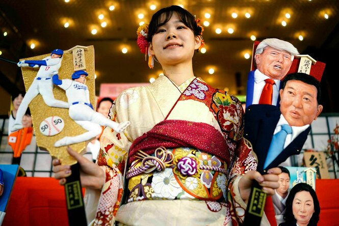 Eine Frau in trägt ein traditionelles japanisches Gewand und hält traditionelle Puppen in den Händen, eine zeigt Donald Trump, eine weitere Shigeru Ishiba