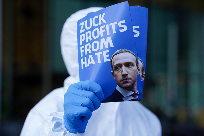 Eine Person hält ein Protestplakat in die Höhe auf dem steht "Zuck profits from hate"