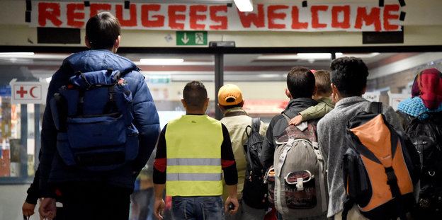 Menschen von hinten stehen vor einem Schild mit der Aufschrift "Refugees welcome"