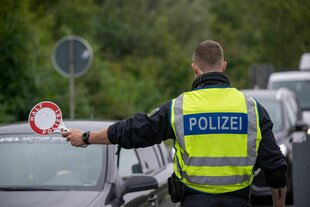 Ein Polizist hält Fahrzeuge an der Grenze zu Deutschland an