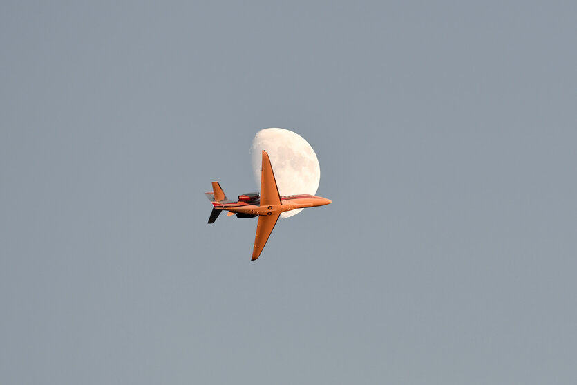 Ein Privatjet am Himmel vor dem Mond.