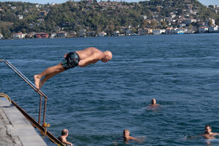 Ein äterer Mann springt kopfüber in den Bosporus, unten erwarten ihn Schwimmer