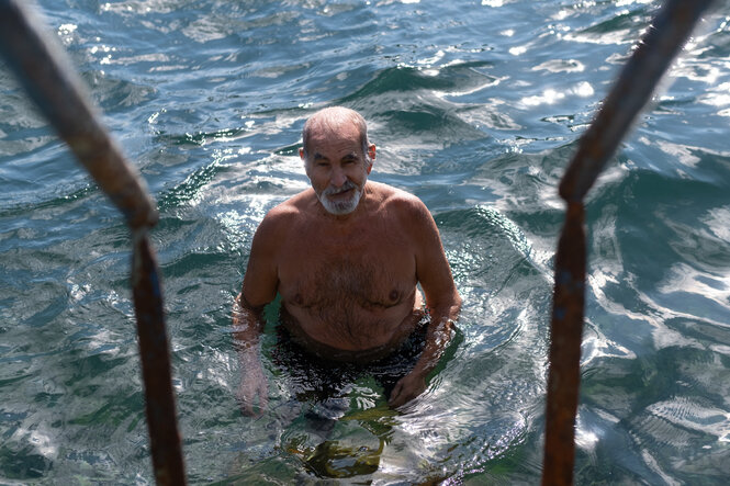 Ein äterer Mann steht im Wasser an einer Eisentreppe