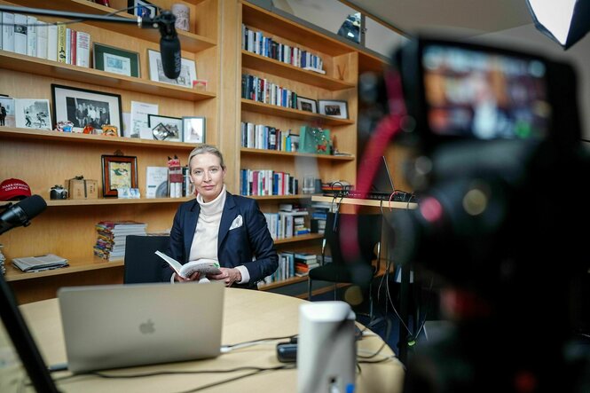 Alice Weidel sitzt an einem Tisch vor einer Kamera und Mikrofonen