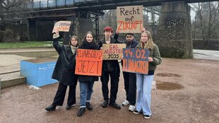 Protestierende posen mit Plakaten vor der Presse.