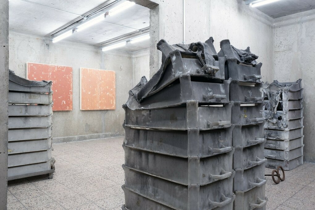 In einem Ausstellungsraum sind hohe Stapel aus Transportkisten aus Plastik aufgestellt. Die Stapel in Hell- und Dunkelgrau sind ineinander zusammengeschmolzen.