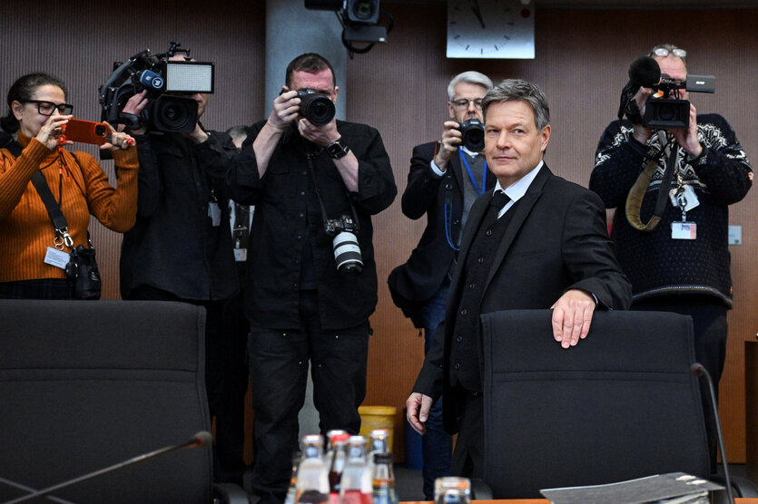 Robert Habeck steht hinter einem Stuhl, hinter ihm Fotografen