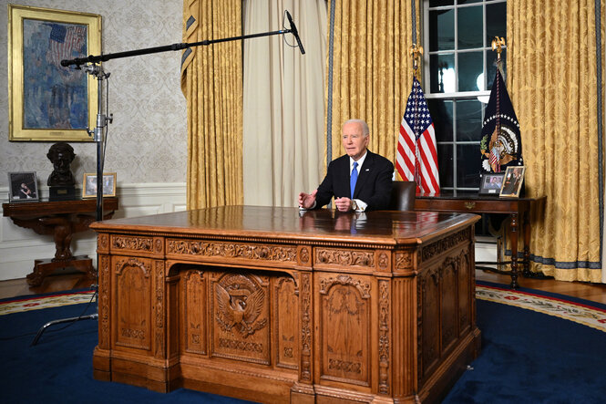 Joe Biden hinter dem großen Holztisch im Oval Office, über ihm hängt ein Mikrofon