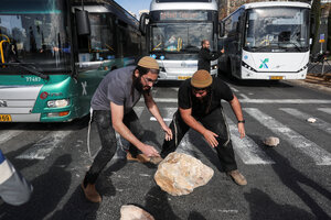 Junge Männer rollen einen großen Stein als Blockade auf eine Straße.