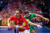 Dänischer Handballer enteilt mit dem Ball in der Hand seinem algerischen Gegenspieler